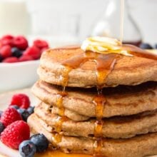 close up image of stack of four pancakes with syrup dripping down