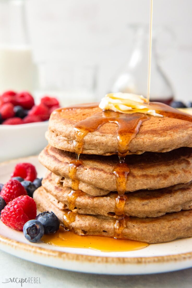 close up image of stack of four pancakes with syrup dripping down