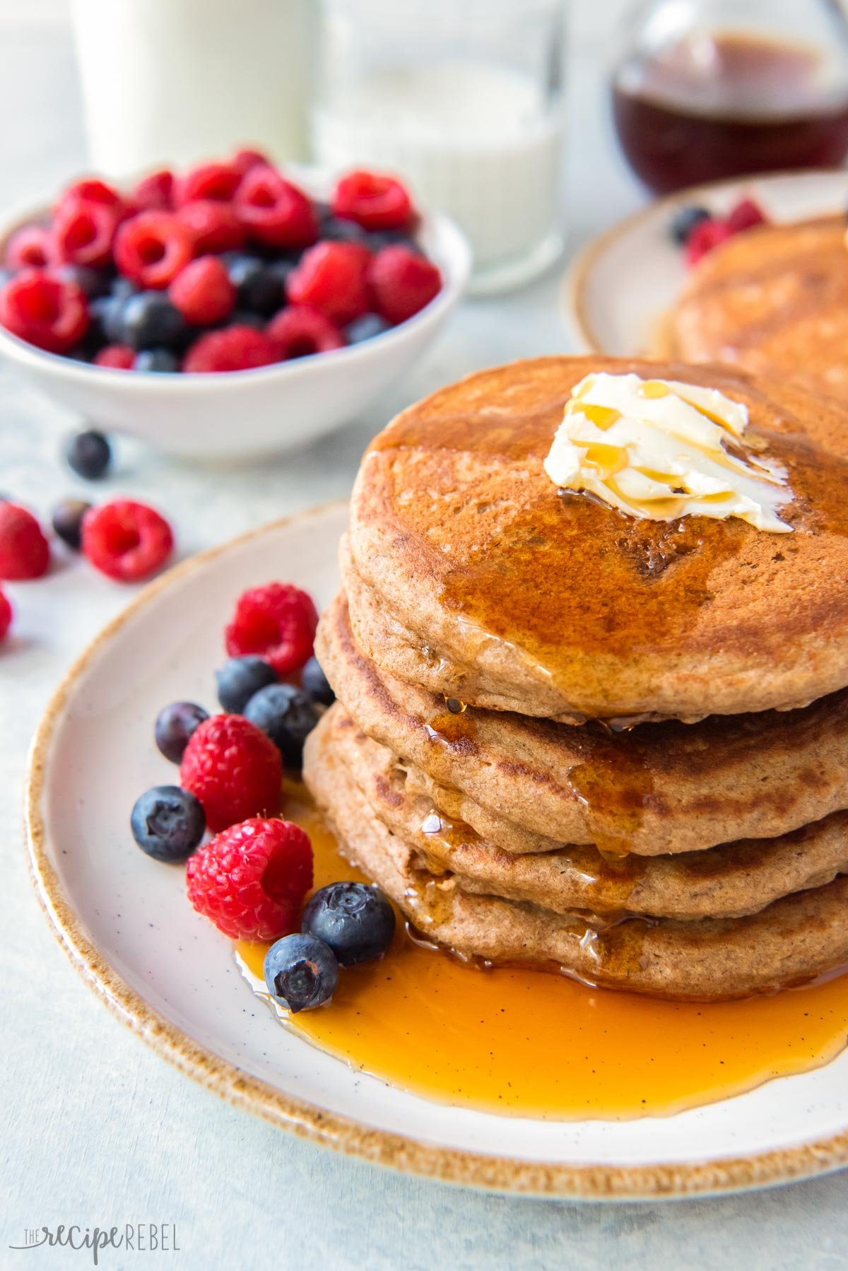 stack of pancakes on white plate with berries and syrup