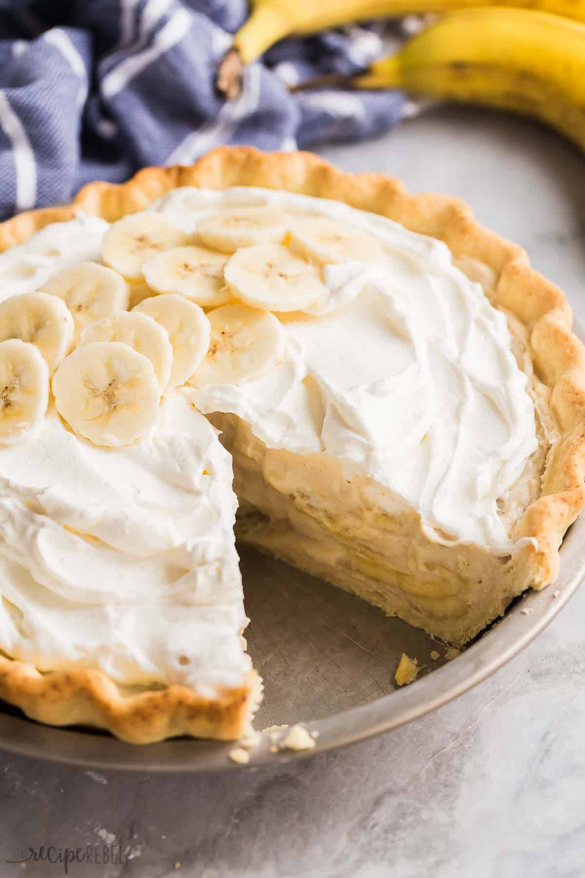 banana cream pie piece missing in tin pie plate with whipped cream and fresh banana slices on top