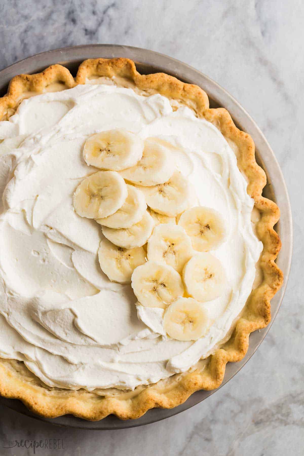 banana cream pie whole overhead on grey marble with fresh banana slices on top