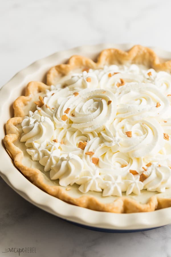 coconut cream pie whole with whipped cream roses on marble background