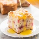 square image of vanilla sauce being poured over piece of rhubarb cake on plate.