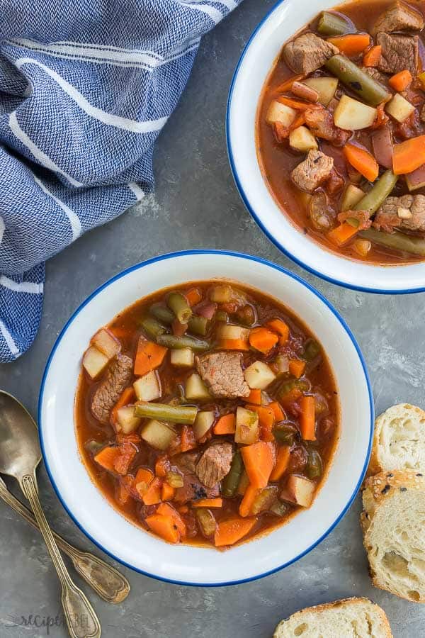 This crockpot Vegetable Beef Soup is a hearty, healthy soup recipe -- loaded with chunks of tender beef and lots of veggies! Perfect for your weekend meal prep and freezer friendly. #soup #healthyrecipe #recipe #slowcooker #crockpot overhead crockpot vegetable beef soup two white bowls with blue rims with crusty bread on the side