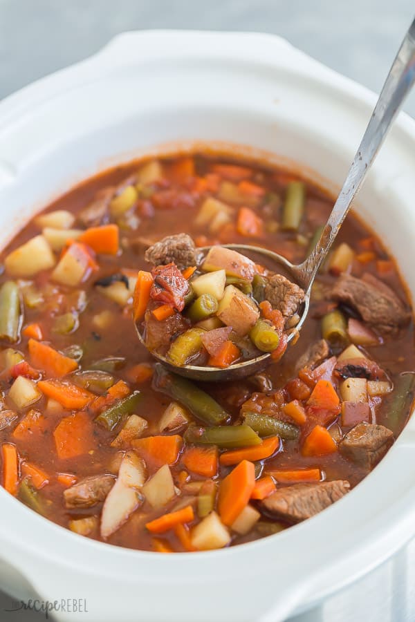 This crockpot Vegetable Beef Soup is a hearty, healthy soup recipe -- loaded with chunks of tender beef and lots of veggies! Perfect for your weekend meal prep and freezer friendly. #soup #healthyrecipe #recipe #slowcooker #crockpot crockpot vegetable beef soup in slow cooker with metal scoop pulling some out