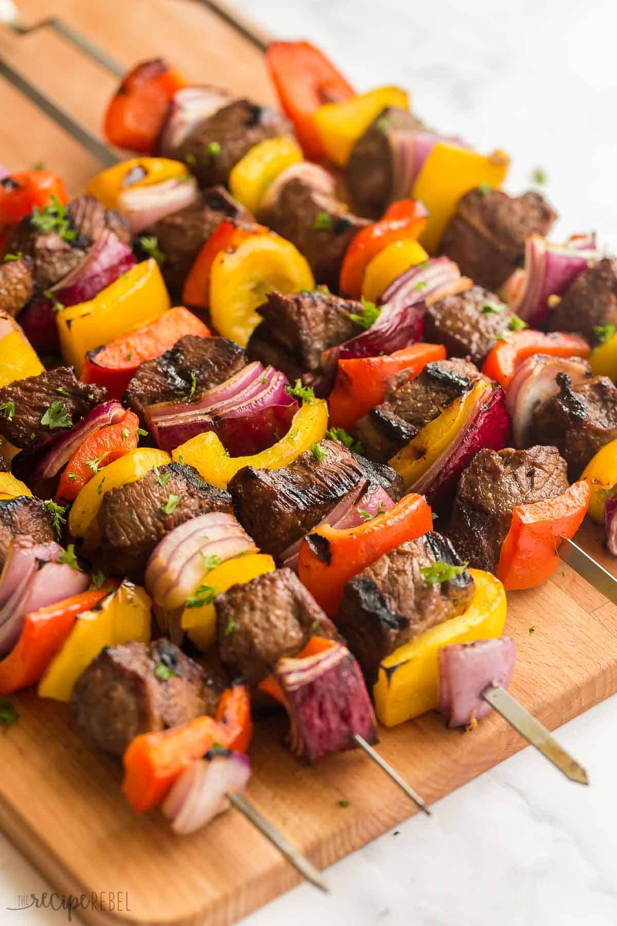 These Steak Kabobs are made with an easy marinade and loaded with tender steak, bell peppers and red onions. Easy to make and easy to prep ahead for summer entertaining! #steak #grilling #summer #recipe | summer recipes | summer dinner | grilling recipe | grilled steak | steak skewers | shish kabobs | kebabs | easy dinner ideas steak kabobs on wooden cutting board with vegetables.