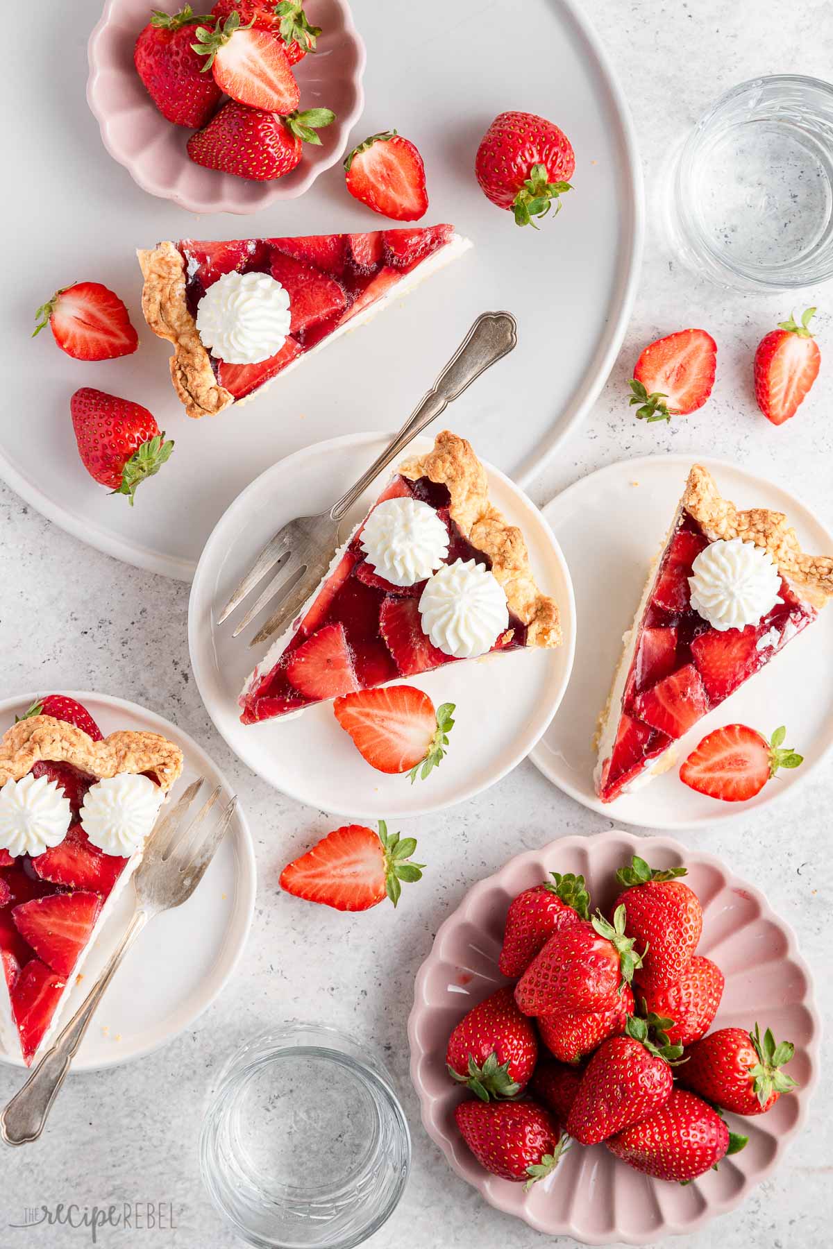 several pieces of strawberry pie on white plates with strawberries all around.