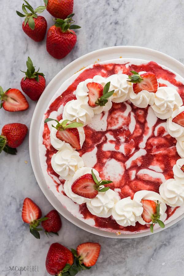 strawberry shortcake ice cream cake overhead with whipped cream and halved strawberries on grey marble background