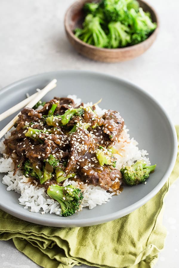 plate of Asian beef and broccoli over white rice on grey plate with broccoli in the background