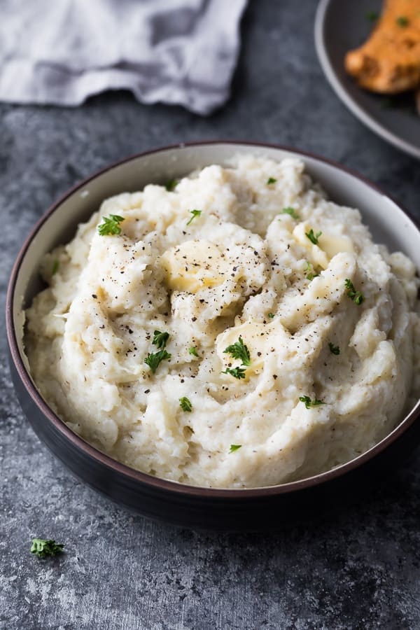 instant pot mashed cauliflower in black bowl on grey background with butter on top