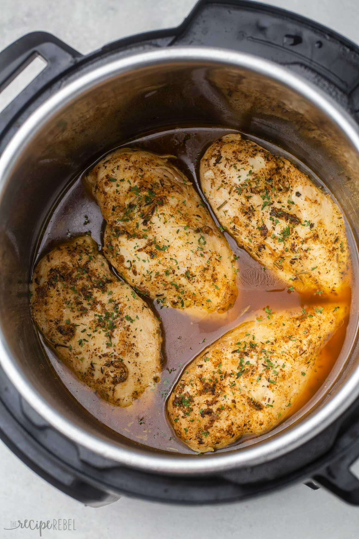 chicken breasts in instant pot with juices and seasoning.