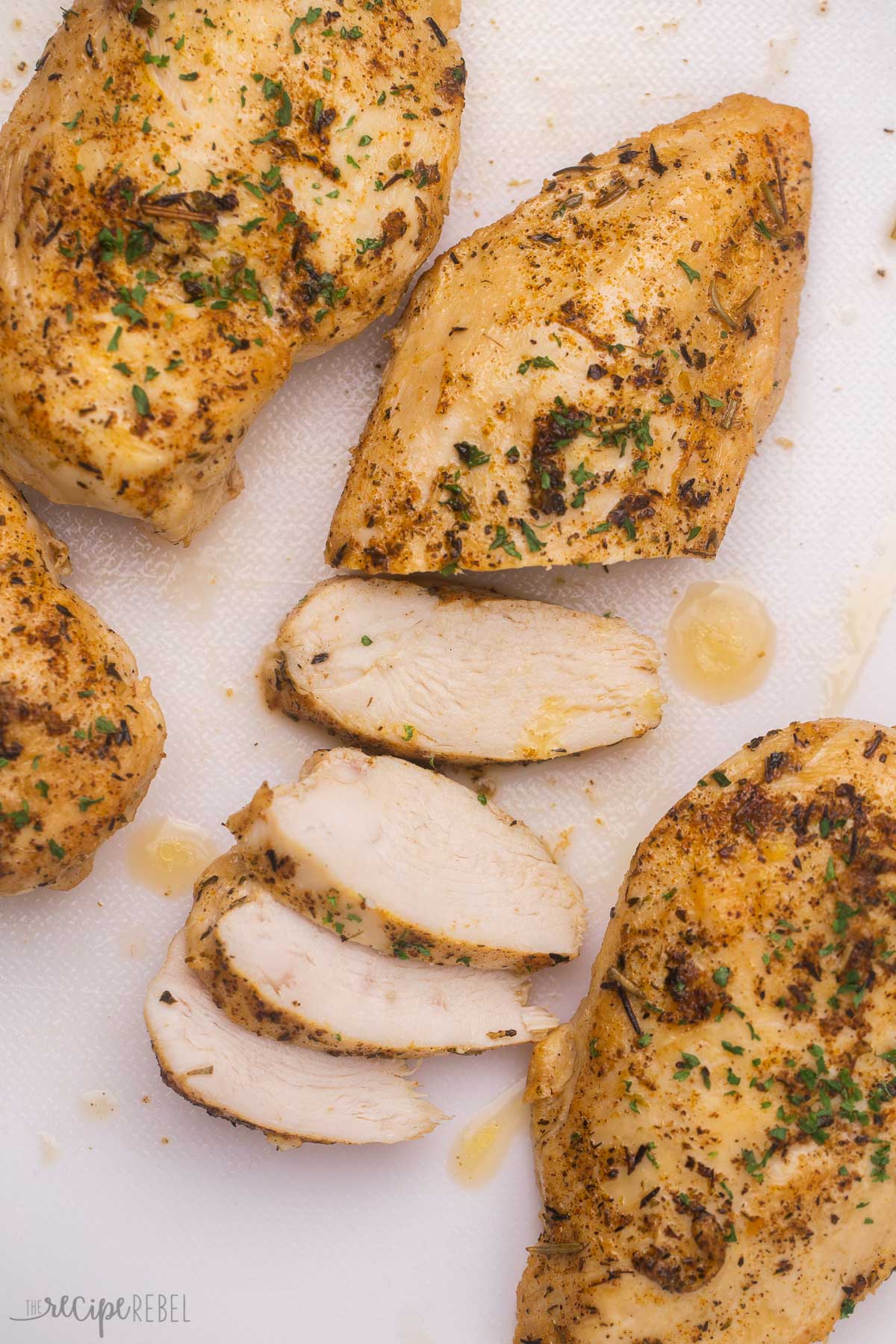 chicken breast partially sliced on white cutting board with whole chicken breasts on the side.