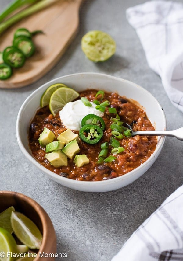 instant pot vegetarian chili in white bowl with jalapenos avocado green onions and lime wedges