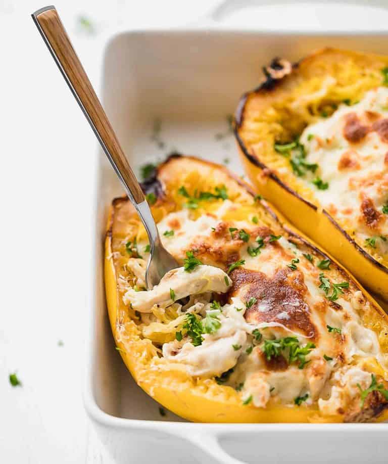 chicken alfredo spaqhetti squash boats in white baking dish with fork stuck in filling