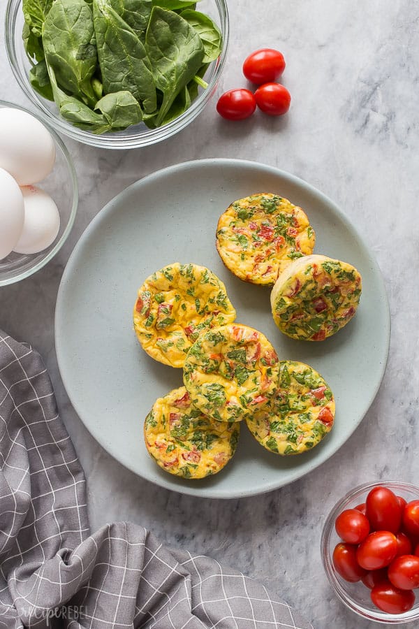 frittata muffins on plate overhead with eggs in shell spinach and cherry tomatoes around the edges