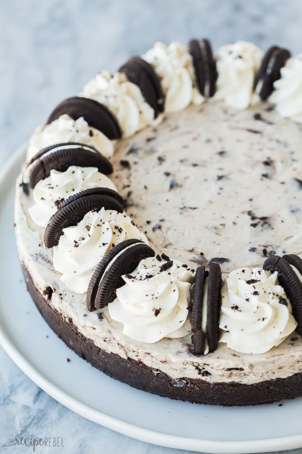 no bake oreo cheesecake whole on white plate with whipped cream swirls and halved oreos on marble background