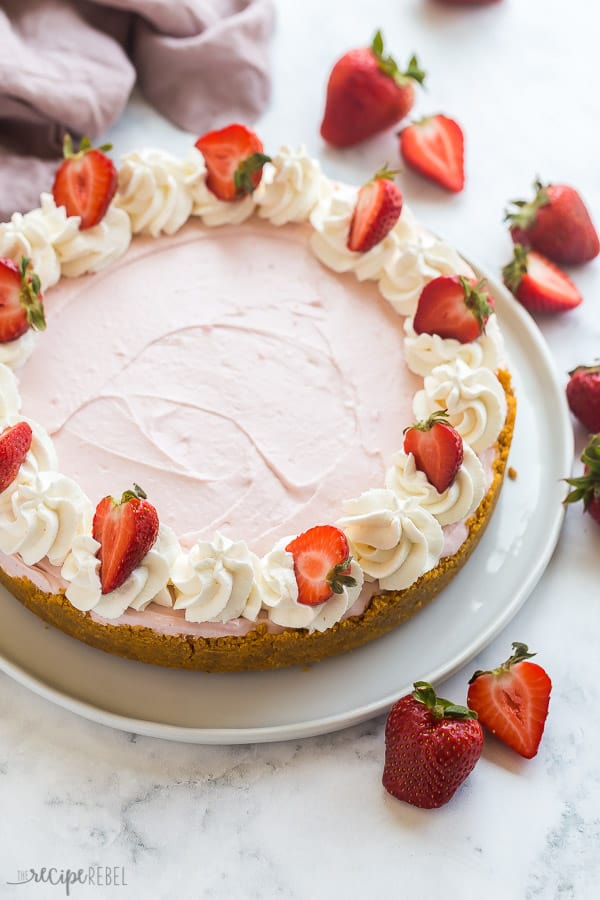 This no bake Strawberry Cheesecake is light, fluffy and loaded with fresh strawberry puree! Made with fresh or frozen strawberries and don't forget the whipped cream! #cheesecake #strawberry #dessert #recipes no bake strawberry cheesecake whole with whipped cream and fresh strawberries