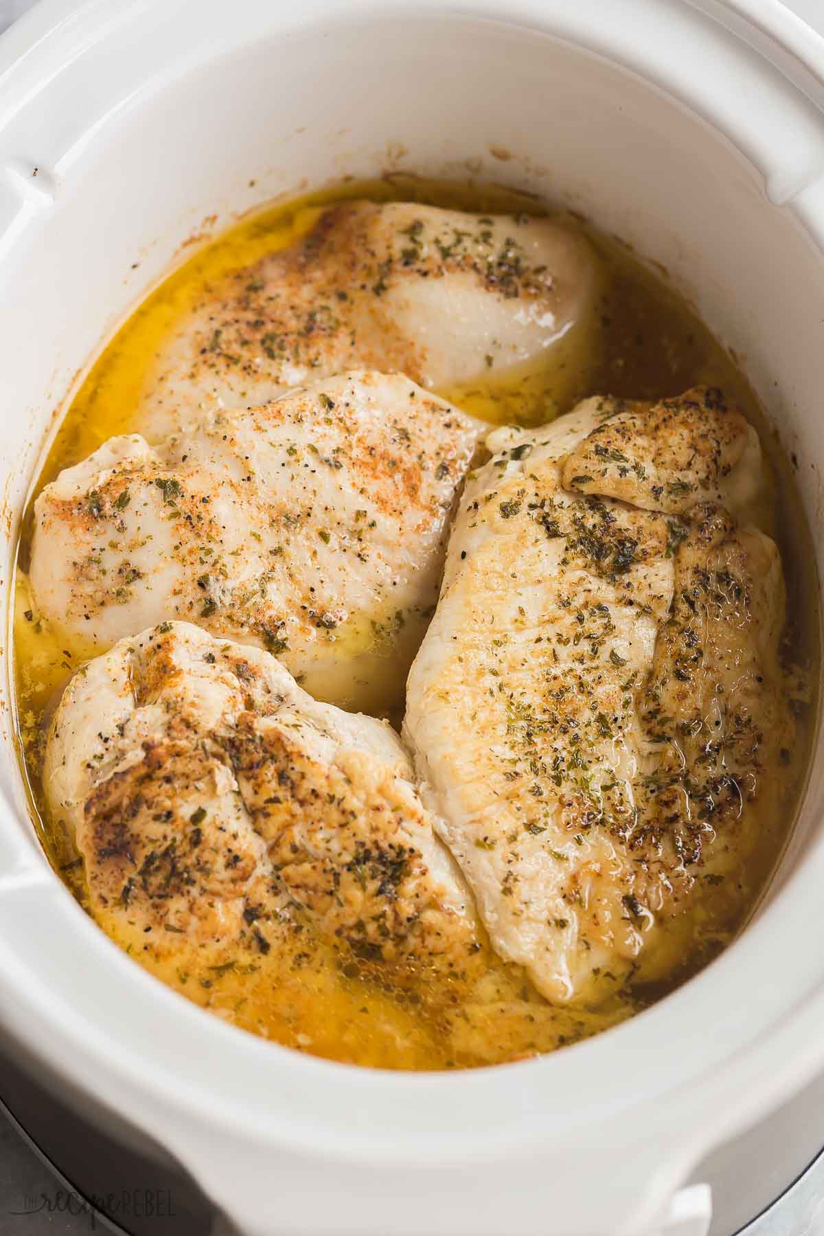 crockpot chicken breast in white slow cooker with juices.