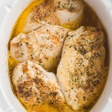 overhead image of four chicken breasts in white slow cooker.