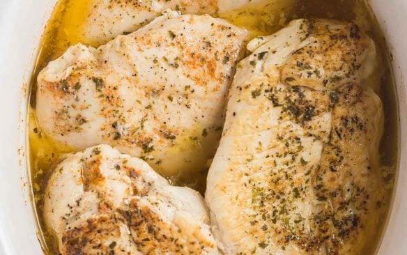 overhead image of four chicken breasts in white slow cooker.