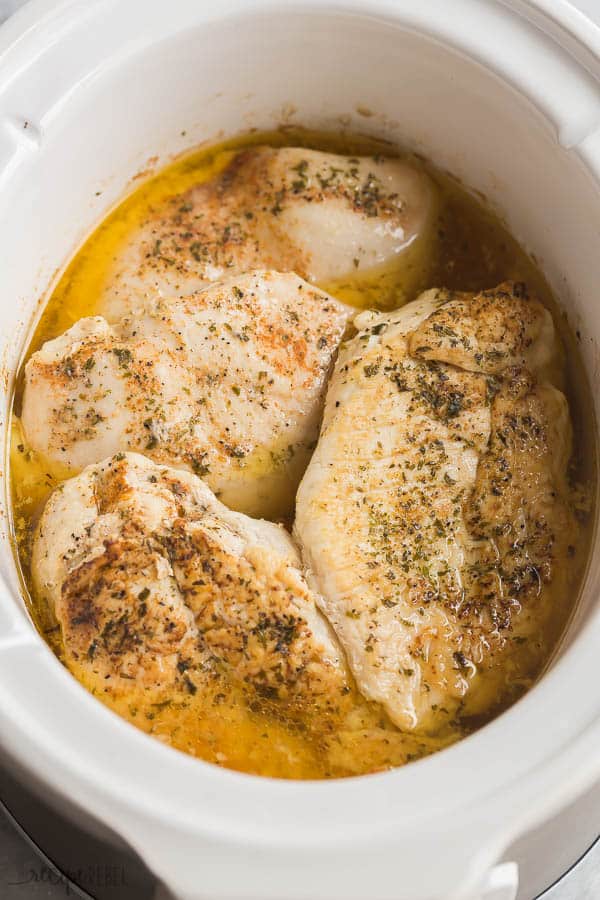 slow cooker chicken breast in white crockpot sitting in broth