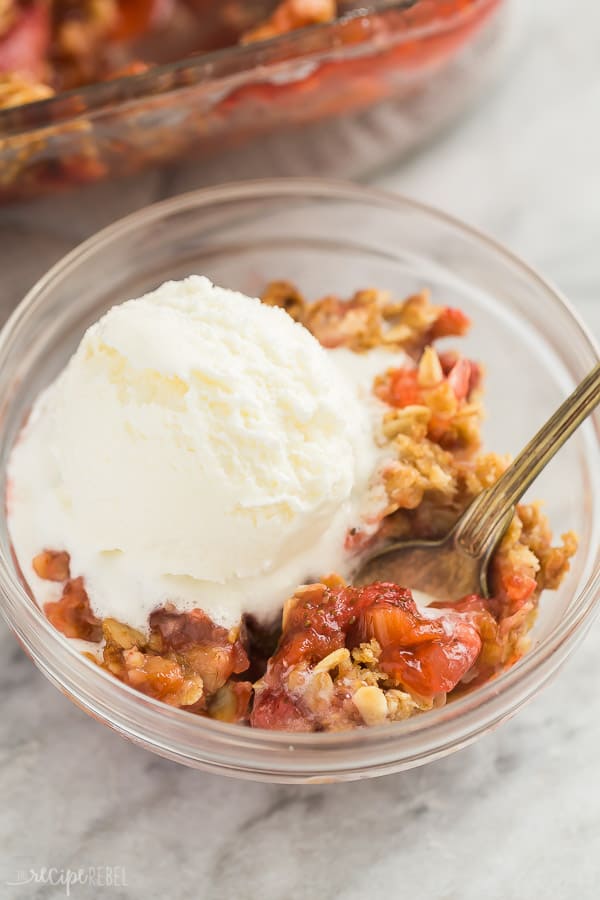 strawberry rhubarb crisp with ice cream close up with spoon stuck in