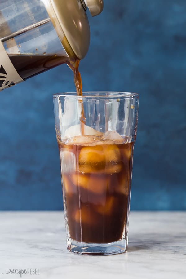 cold brew coffee with ice in a glass being poured out of french press