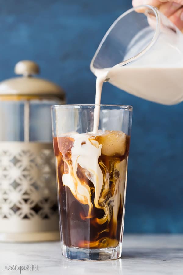 cold brew coffee with cream swirled in glass with french press in background