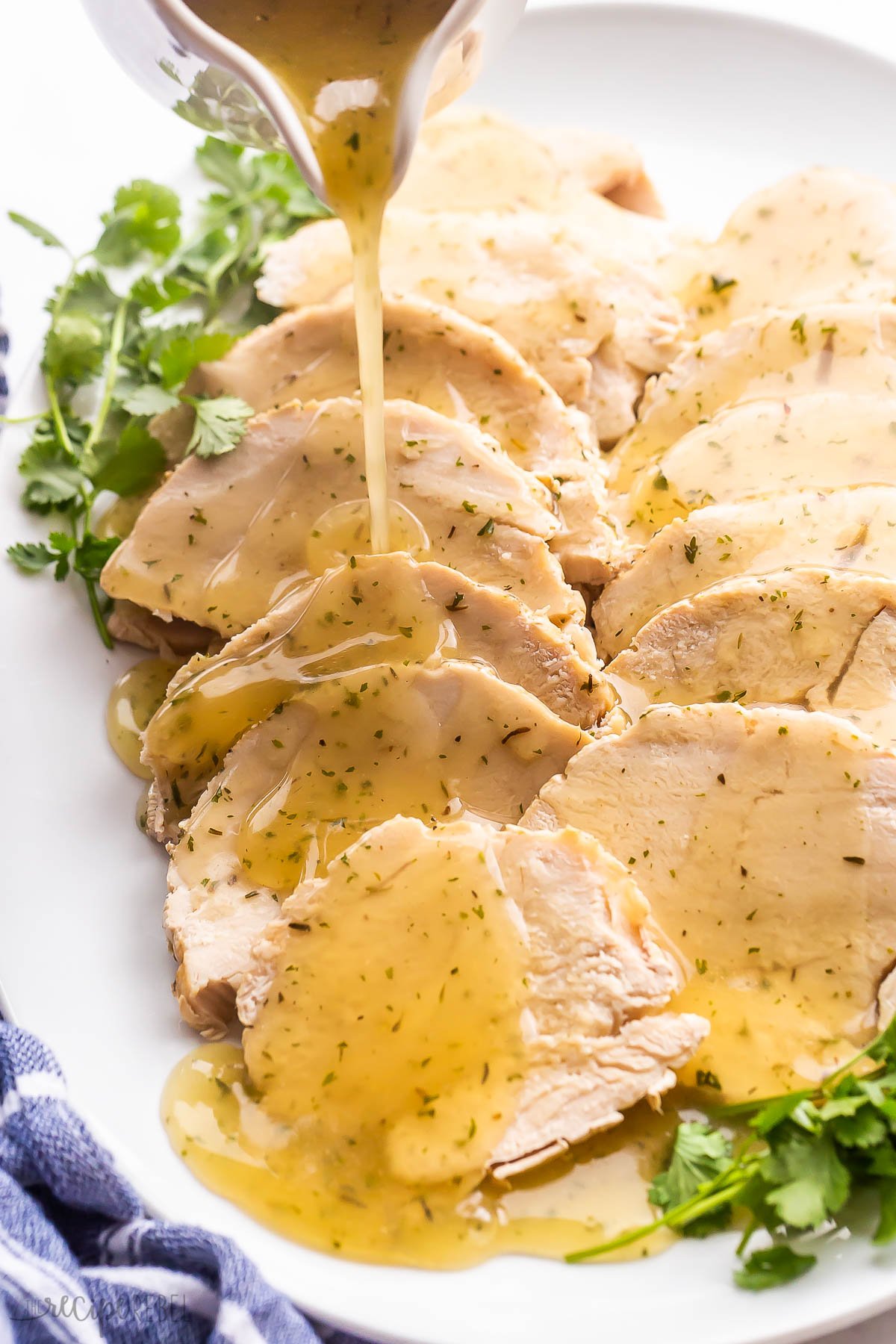 gravy being poured over crockpot turkey breast on white platter.