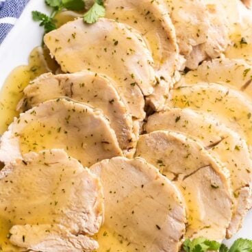 turkey breast slices on white platter with fresh parsley.