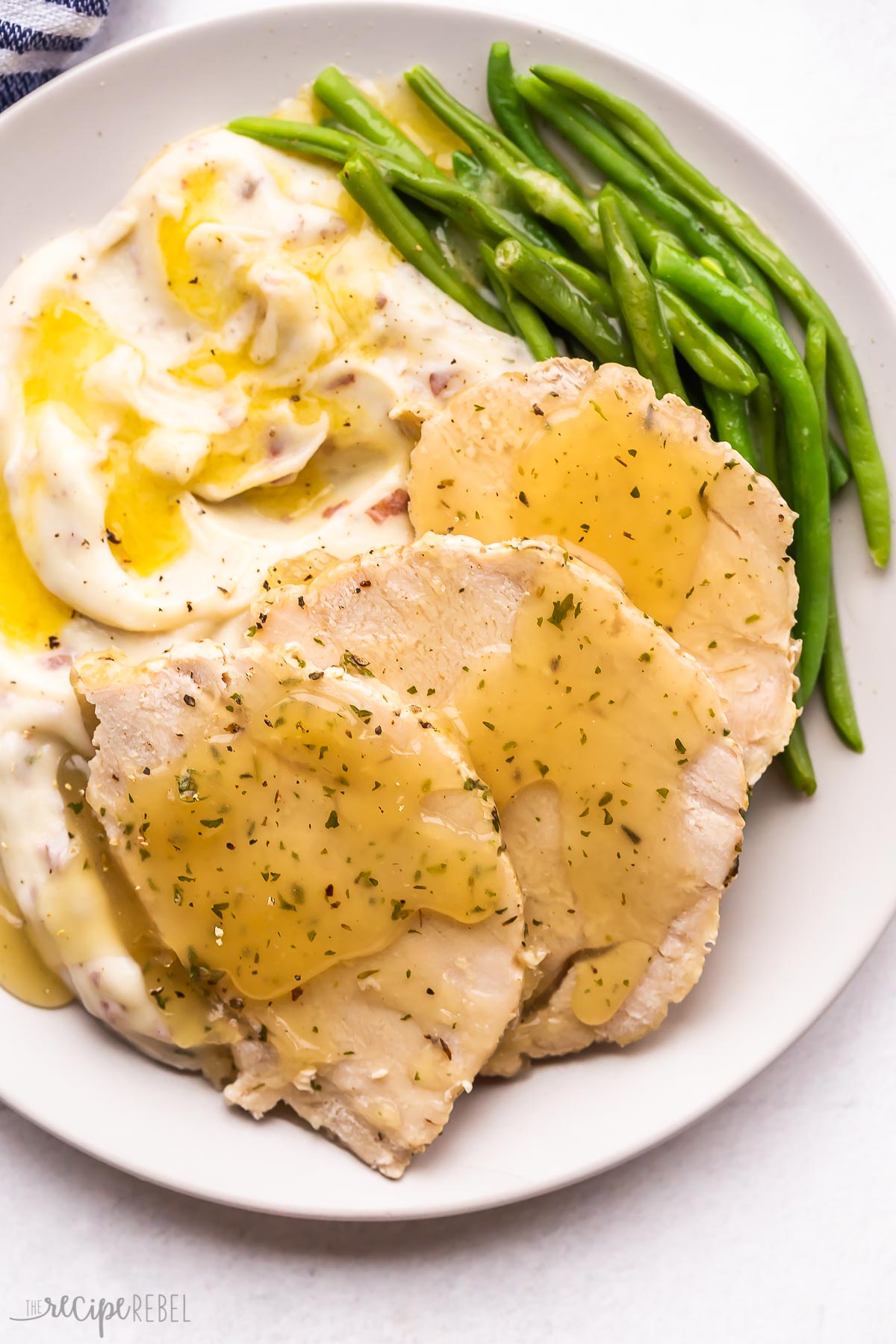 three slices of turkey breast on plate with mashed potatoes and green beans.