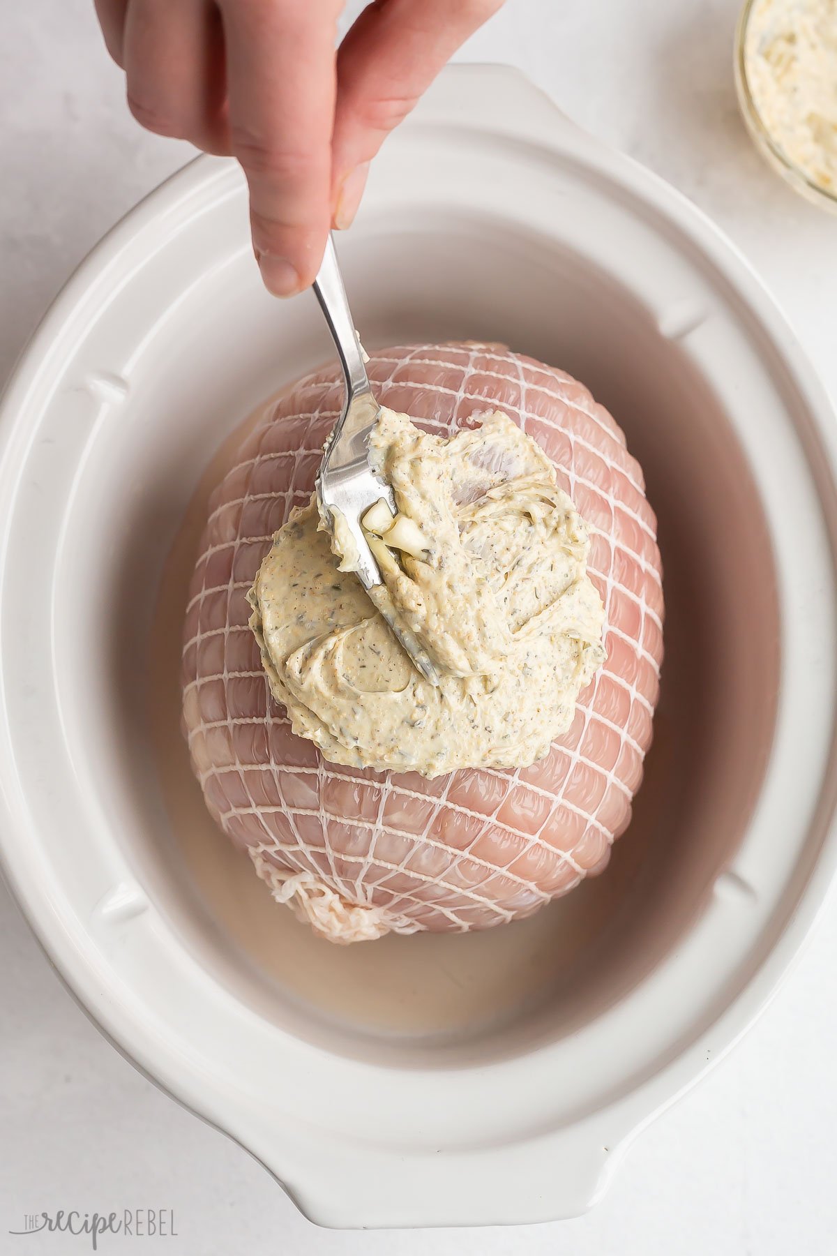 garlic butter being spread over turkey breast roast in slow cooker.