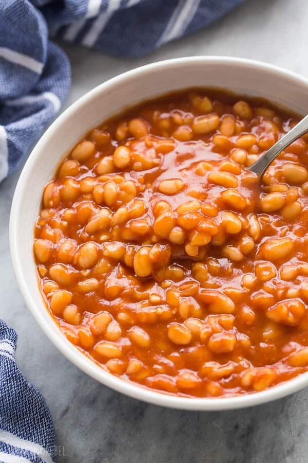 instant pot beans with bbq sauce in a white bowl close up with spoon scooping beans