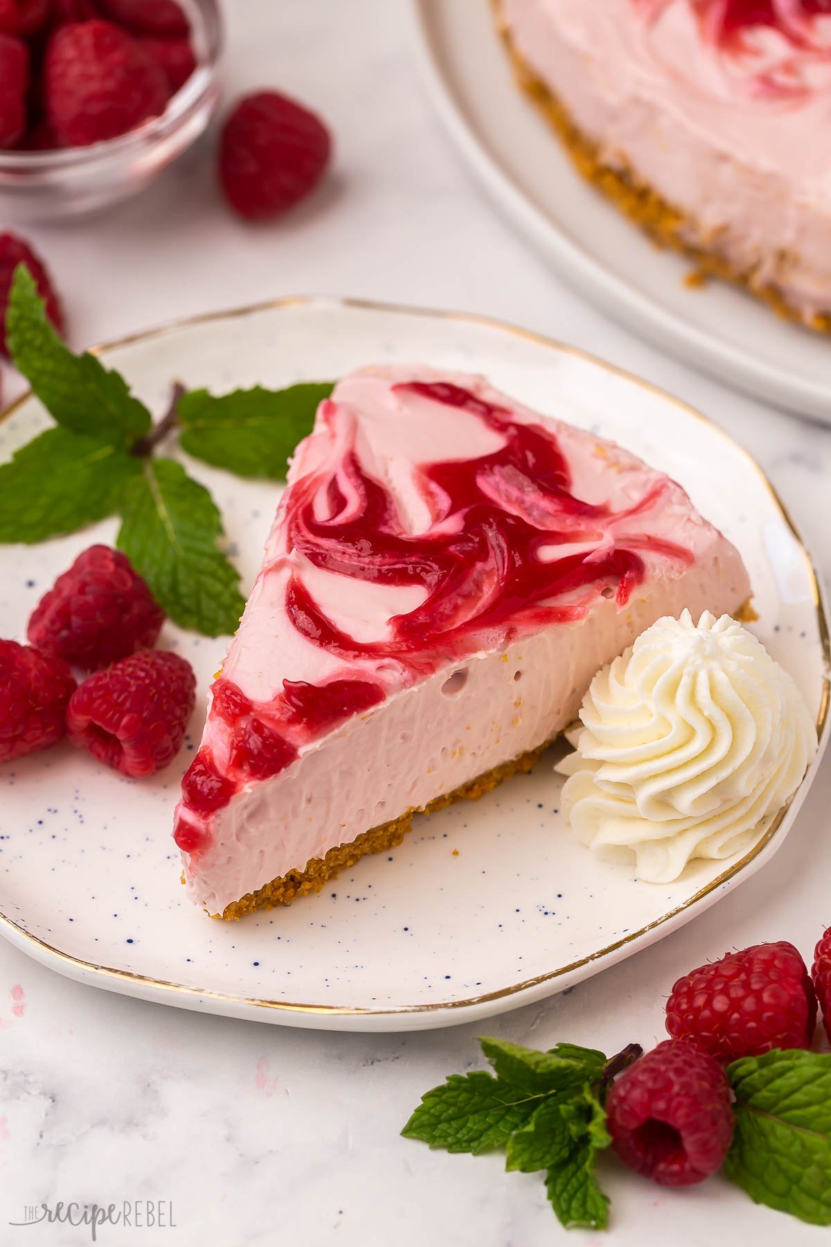 slice of raspberry swirl cheesecake on a white plate with whipped cream.