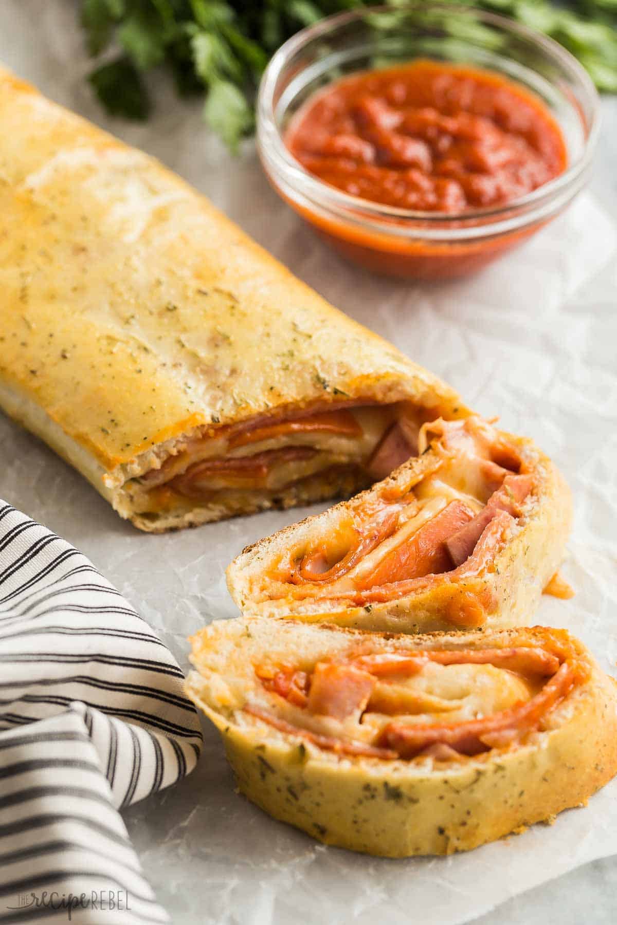 This easy Stromboli recipe is a 30 minute meal that the family will go crazy for! Just a few simple ingredients, prep ahead and freezer friendly! #pizza #dinner #recipe #recipes #easyrecipe Whole stromboli on marble with two slices cut.