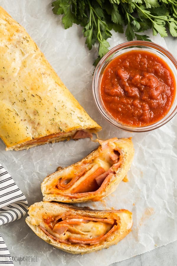 stromboli sliced overhead with two slices cut and a bowl of pizza sauce