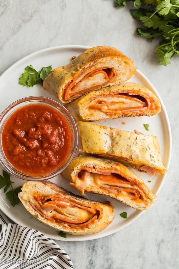 white plate of sliced stromboli with pizza sauce overhead on marble background