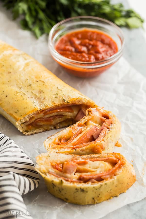 This easy Stromboli recipe is a 30 minute meal that the family will go crazy for! Just a few simple ingredients, prep ahead and freezer friendly! #pizza #dinner #recipe #recipes #easyrecipe stromboli recipe with pizza sauce and two slices cut with fresh parsley in the background