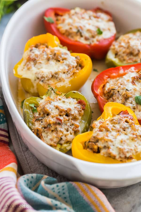 turkey stuffed peppers in white baking dish with multi colored towel on the edge