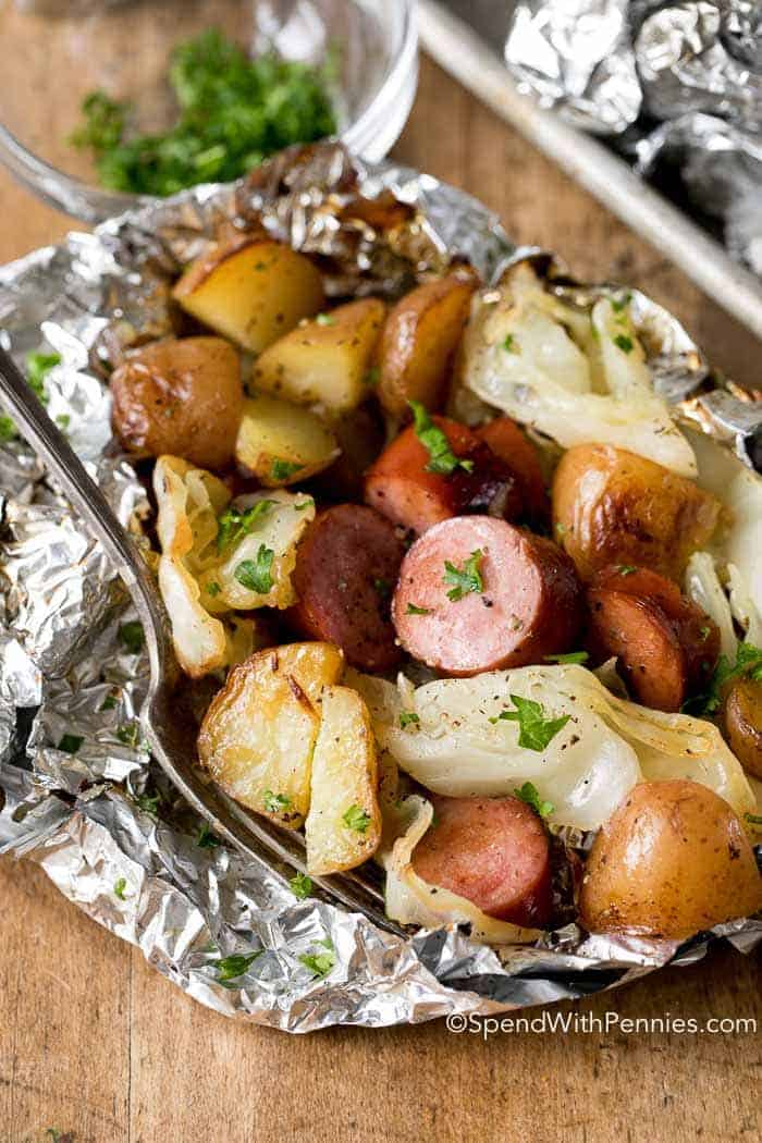 cabbage and sausage foil packs with fork stuck in packet on wood background