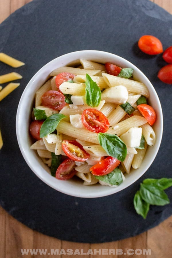 caprese pasta salad overhead in white bowl on black background