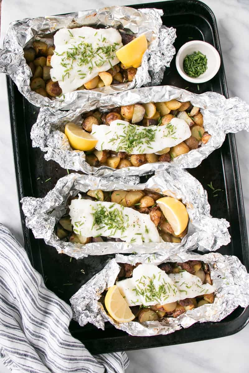 cod chorizo potato packs with fresh lemon wedge lined up on sheet pan