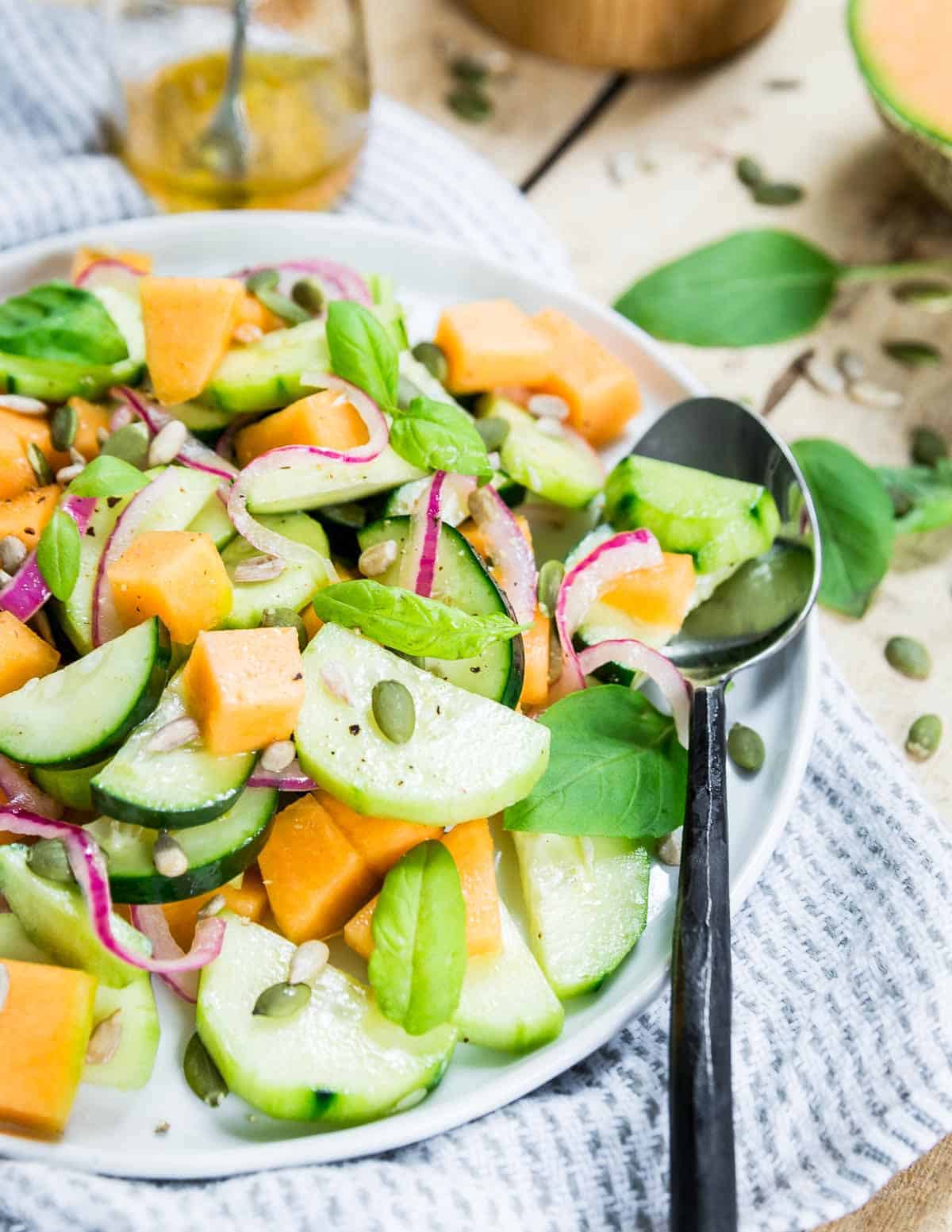 cucumber melon salad on white plate with spoon in salad