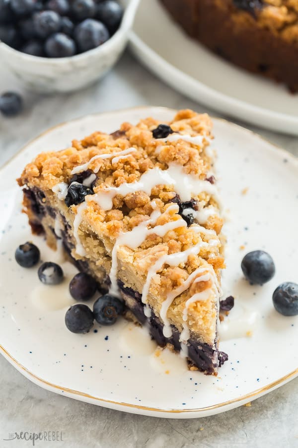 blueberry coffee cake slice with glaze on white speckled plate with fresh blueberries