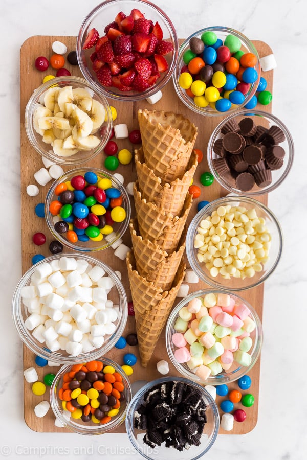 ingredients needed for campfire cones on a board, ice cream cones, marshmallows and candy
