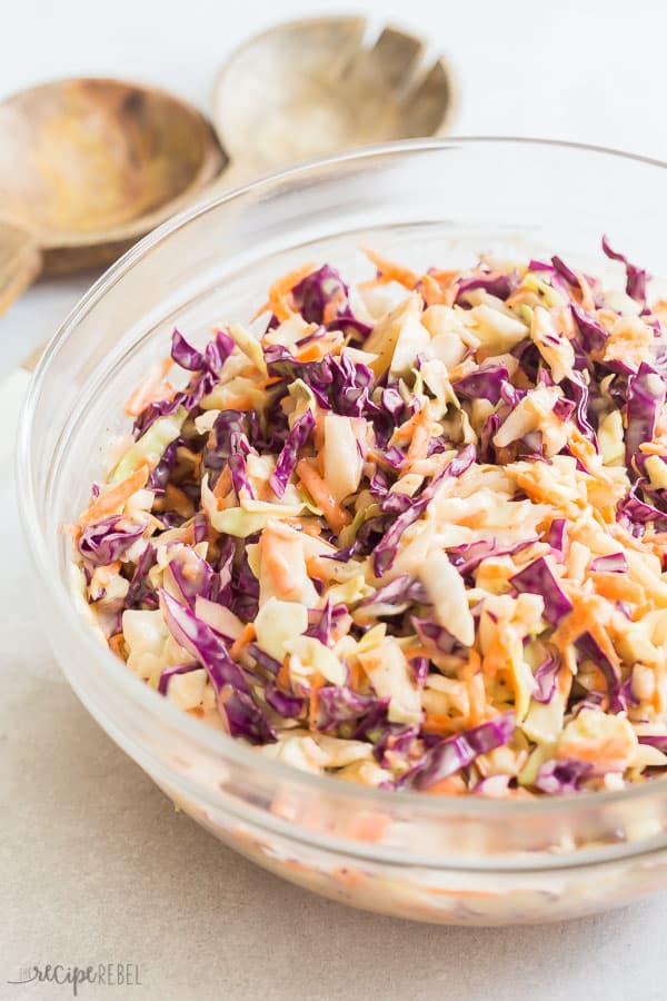 This easy Homemade Coleslaw recipe is way better than store bought! Made with shredded cabbage and a homemade coleslaw dressing everyone loves! #coleslaw #salad #grilling #recipe #dinner #healthy easy homemade coleslaw in glass bowl close up with wooden spoons in the background