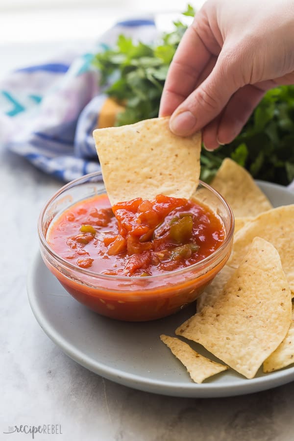 easy salsa recipe with hand scooping salsa with tortilla chip and cilantro in the background