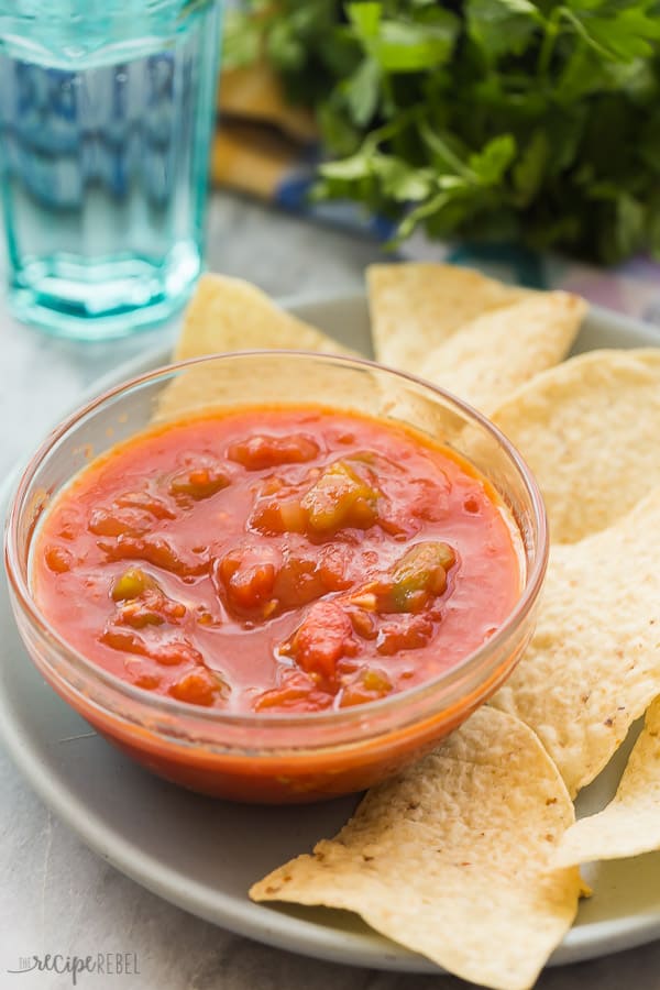 homemade salsa in small glass bowl with tortilla chips on a plate on the side