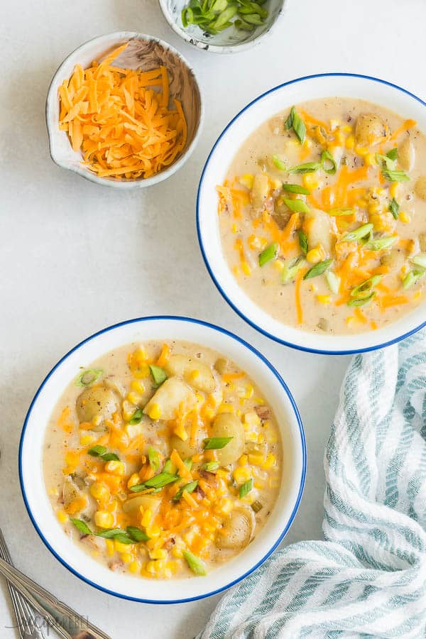 instant pot corn chowder recipe overhead in two white bowls with blue rim and a bowl of shredded cheese