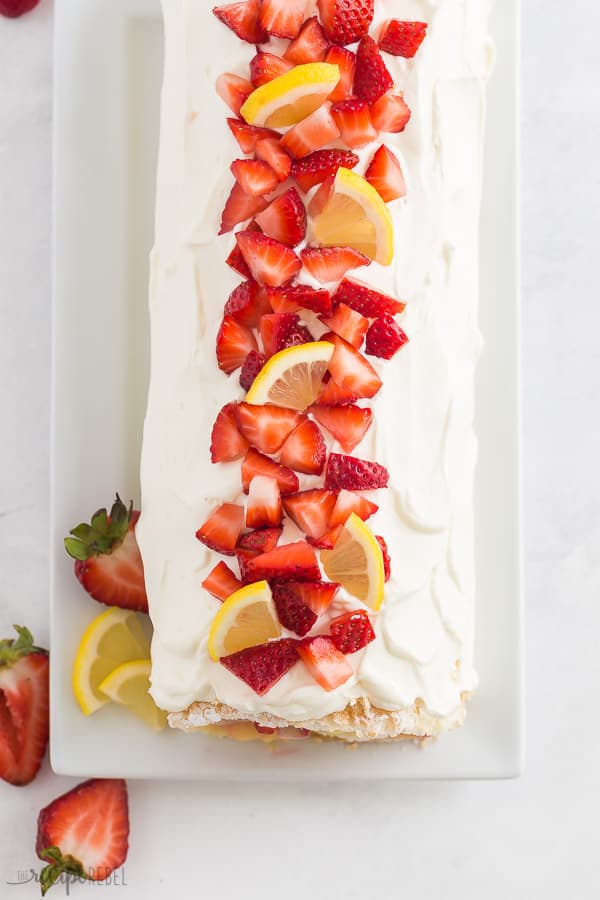 strawberry lemon cake roll overhead whole before slicing with fresh strawberries and lemon wedges on top